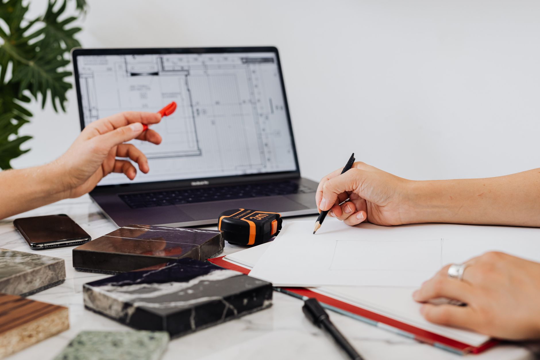 Gros plan sur des mains esquissant des plans de conception avec des échantillons de carrelage et un ordinateur portable, idéal pour les contextes de design d'intérieur.
