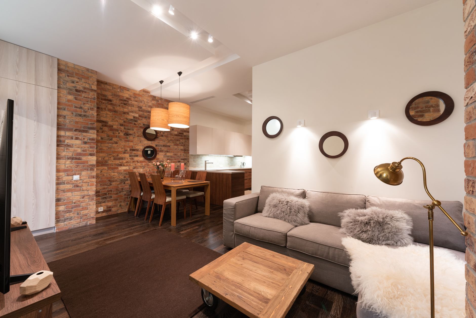 Intérieur d'un appartement avec une table en bois et un canapé avec des coussins près d'une télévision avec une armoire et des murs blancs près de chaises et d'une lampe